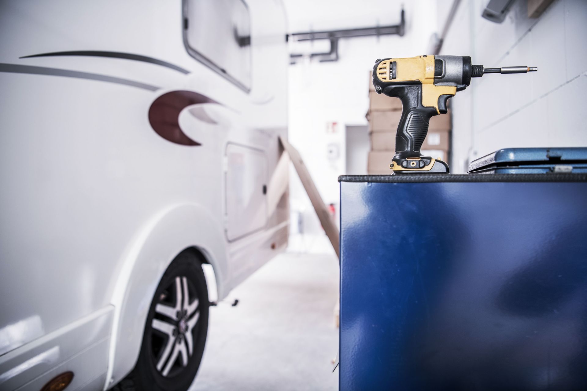 RV being worked on in a shop. A yellow and black drill rests on a blue cabinet.